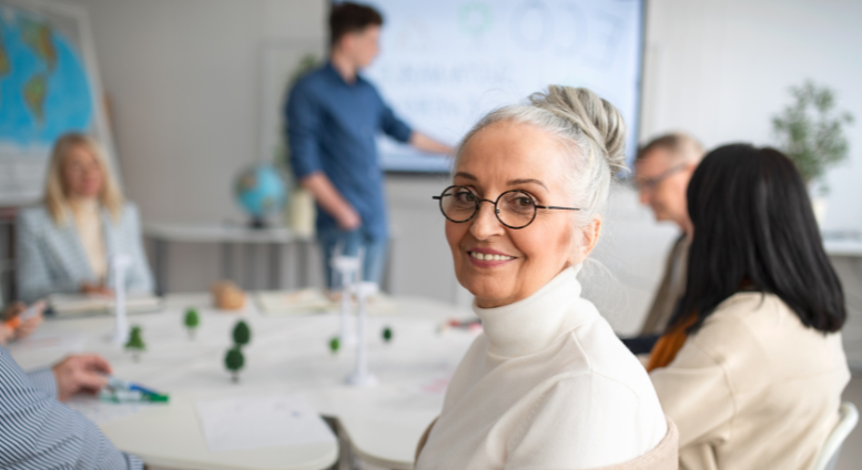 Fem personer i möte runt ett bord. Kvinna som ler.