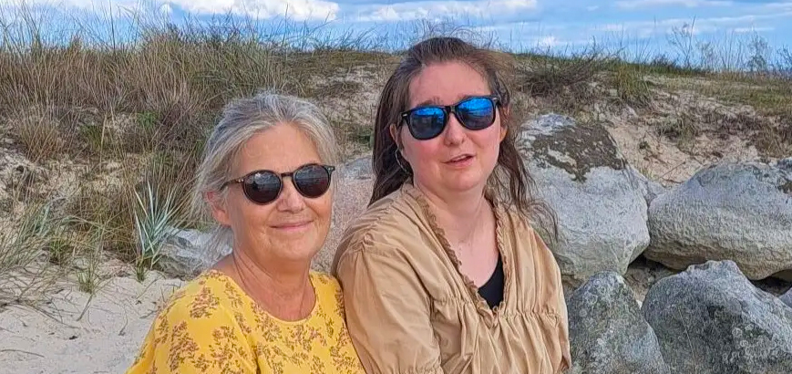 Pernilla Vidingshoff Alling och dottern Tilde sitter i en strandliknande miljö, båda med solglasögon.